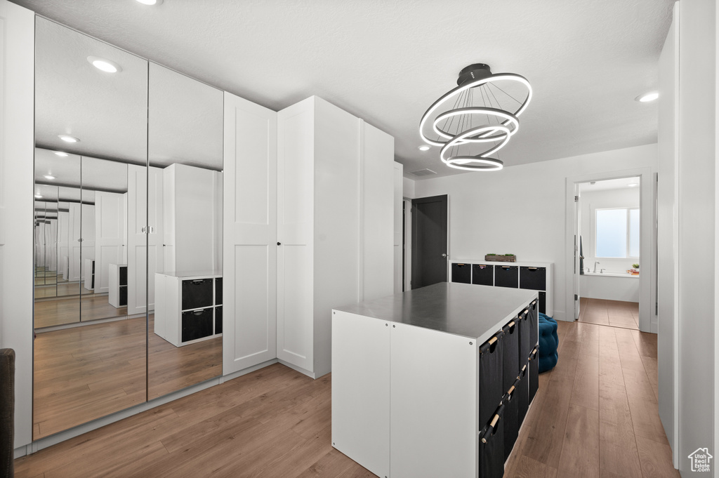 Kitchen featuring light wood finished floors, dark cabinetry, a kitchen island, recessed lighting, and a chandelier