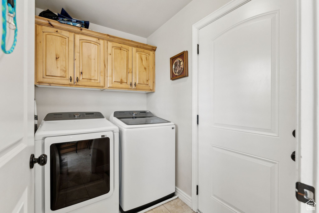 Laundry area featuring washer and clothes dryer, cabinet space, and light tile patterned floors