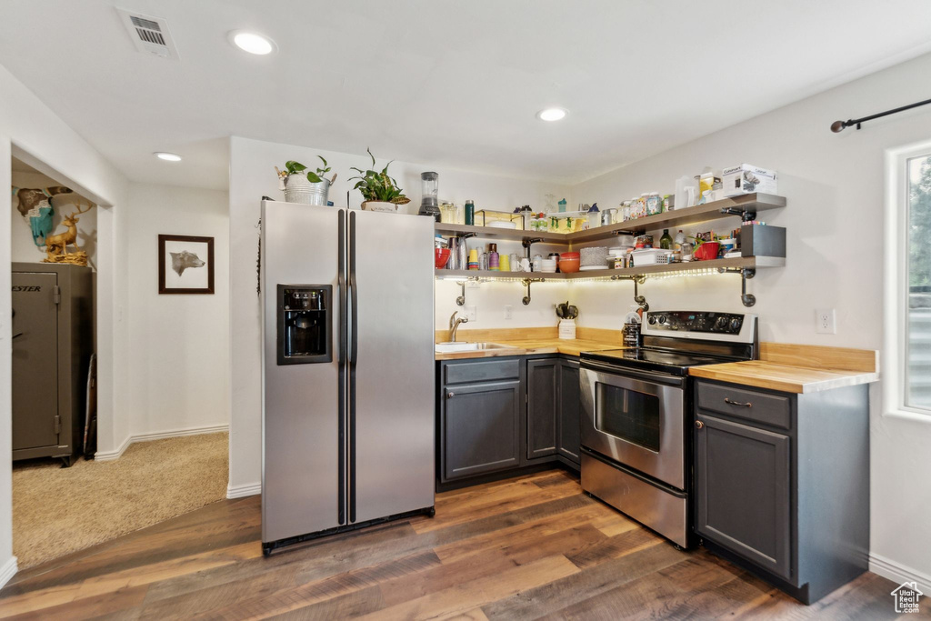 Kitchen featuring stainless steel appliances, open shelves, a sink, wood counters, and recessed lighting
