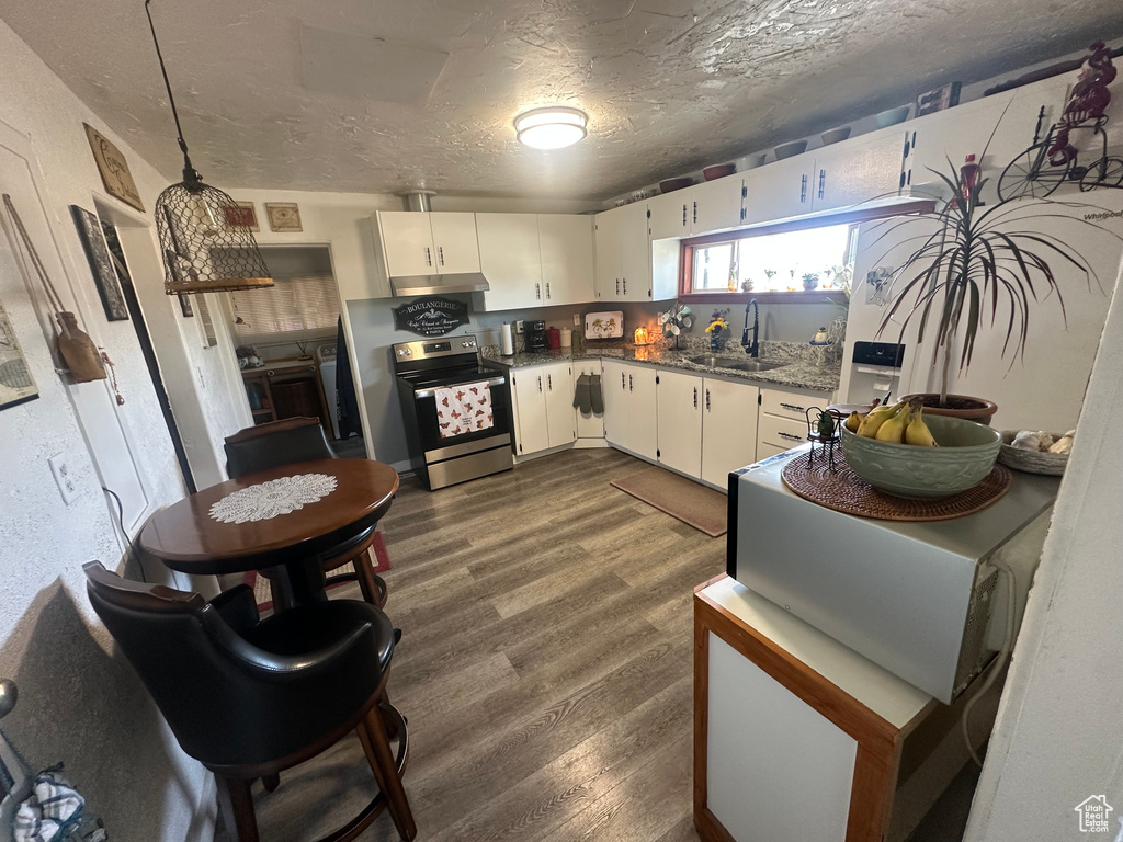 Kitchen with stainless steel electric stove, a sink, under cabinet range hood, dark wood-style floors, and white cabinetry