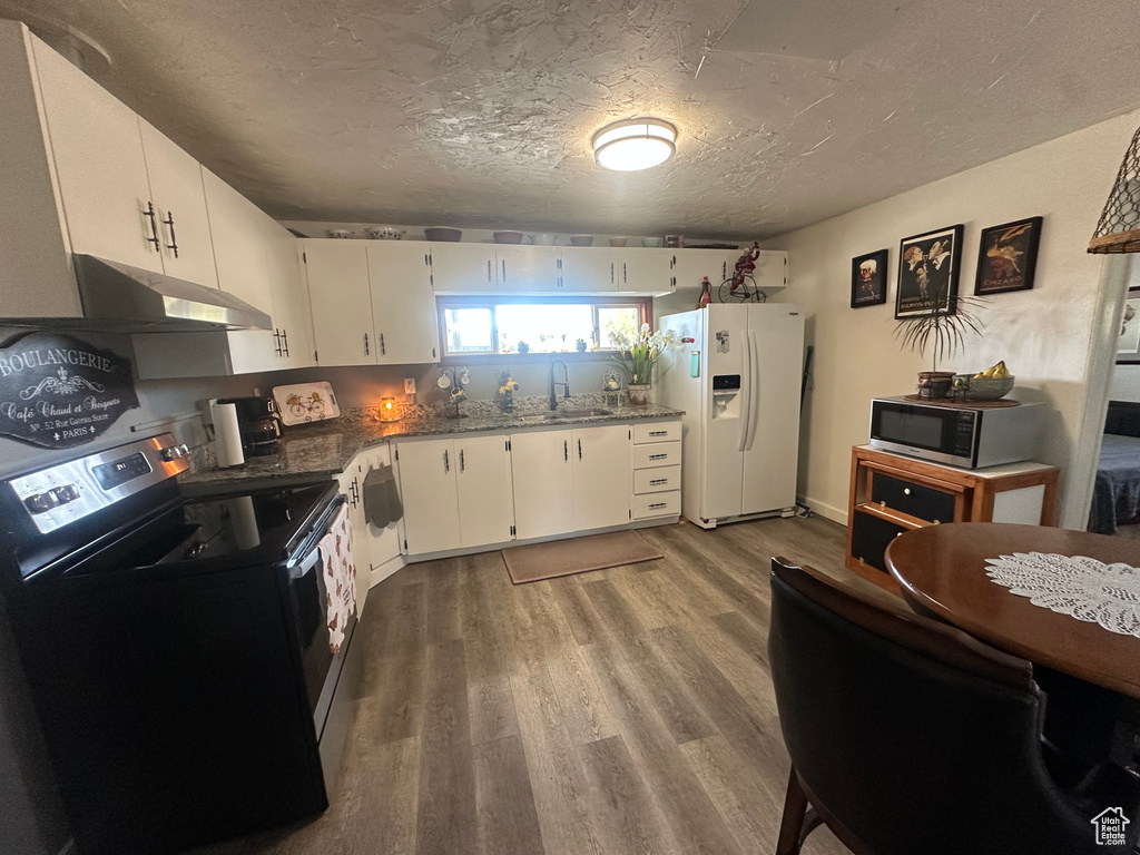 Kitchen featuring white fridge with ice dispenser, black electric range oven, under cabinet range hood, a sink, and wood finished floors