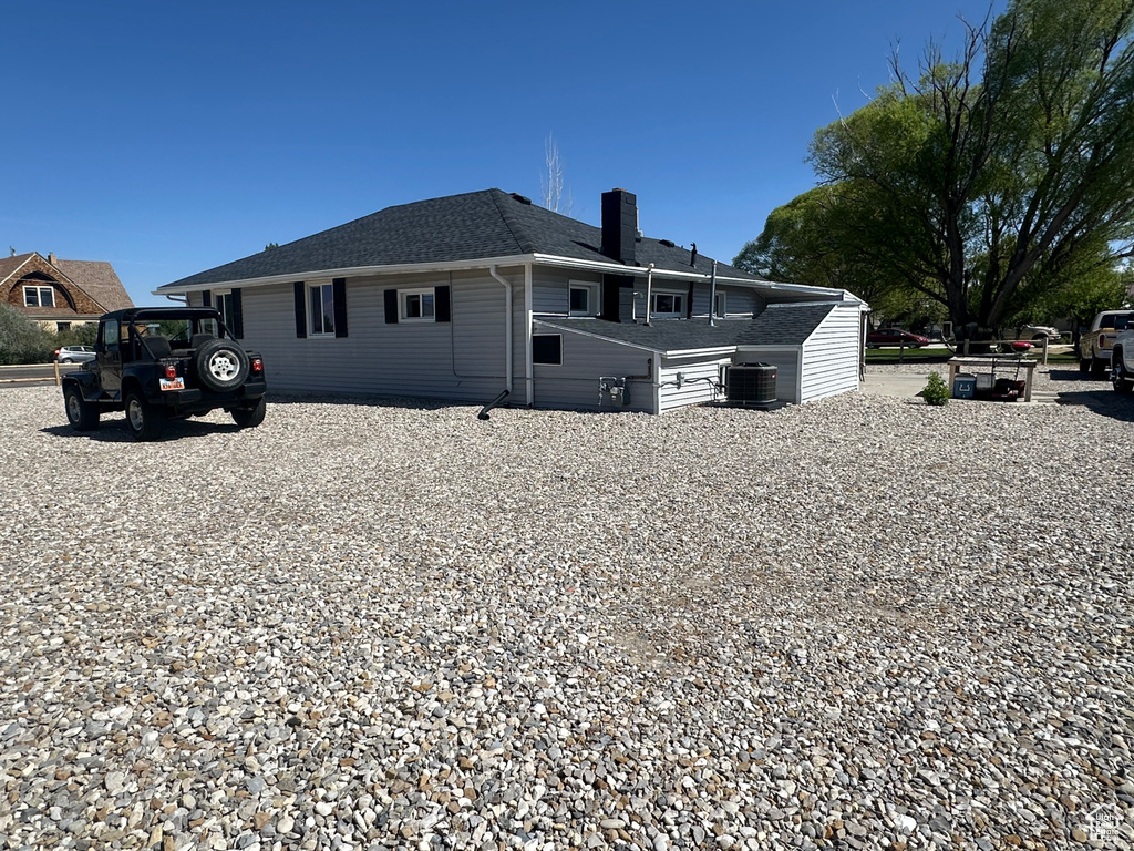 View of side of home featuring a chimney, a shingled roof, and central AC unit