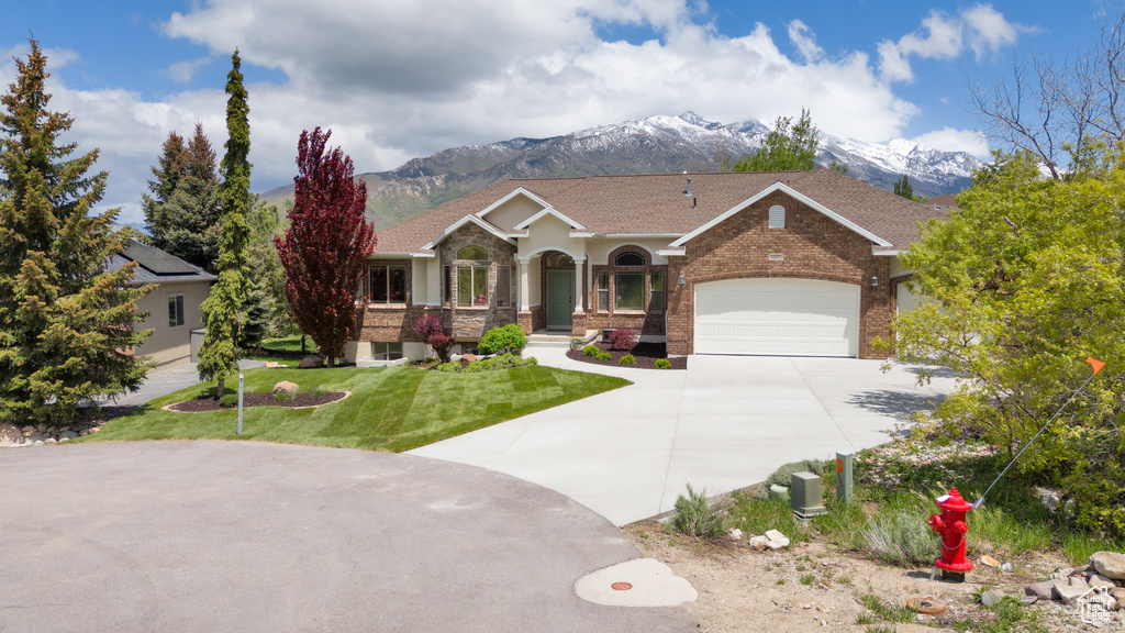 View of front of property featuring a mountain view, concrete driveway, a front lawn, and brick siding
