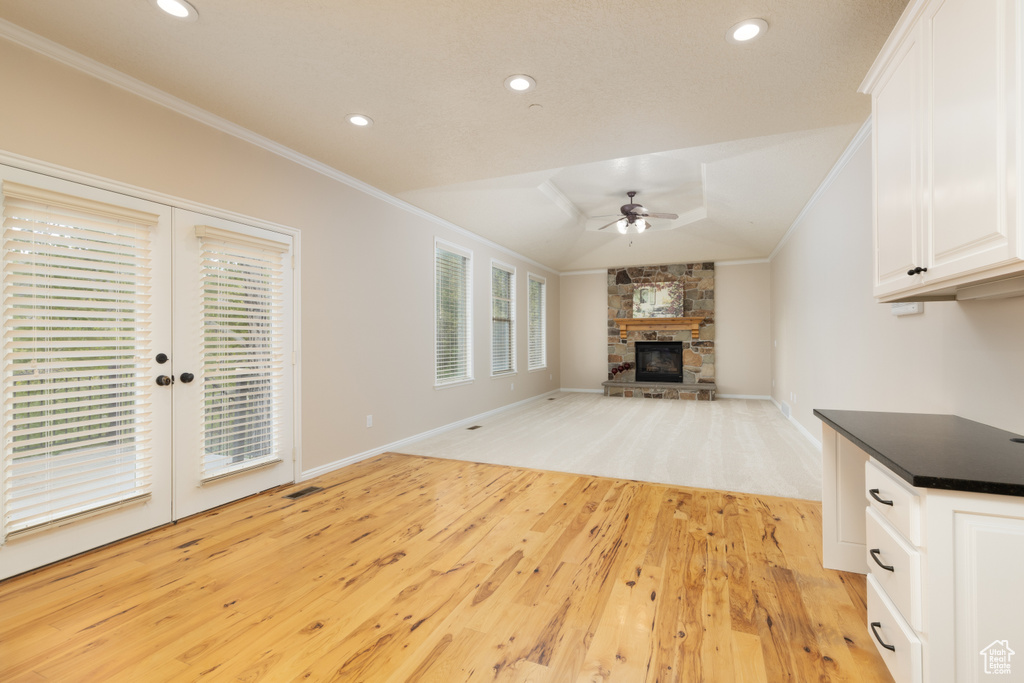 Unfurnished living room featuring ceiling fan, ornamental molding, light wood-style flooring, a stone fireplace, and recessed lighting