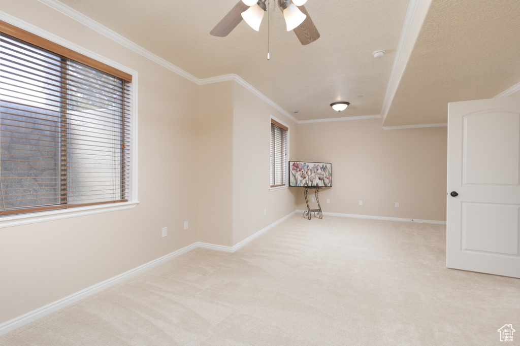 Empty room featuring light colored carpet, ornamental molding, baseboards, and a ceiling fan
