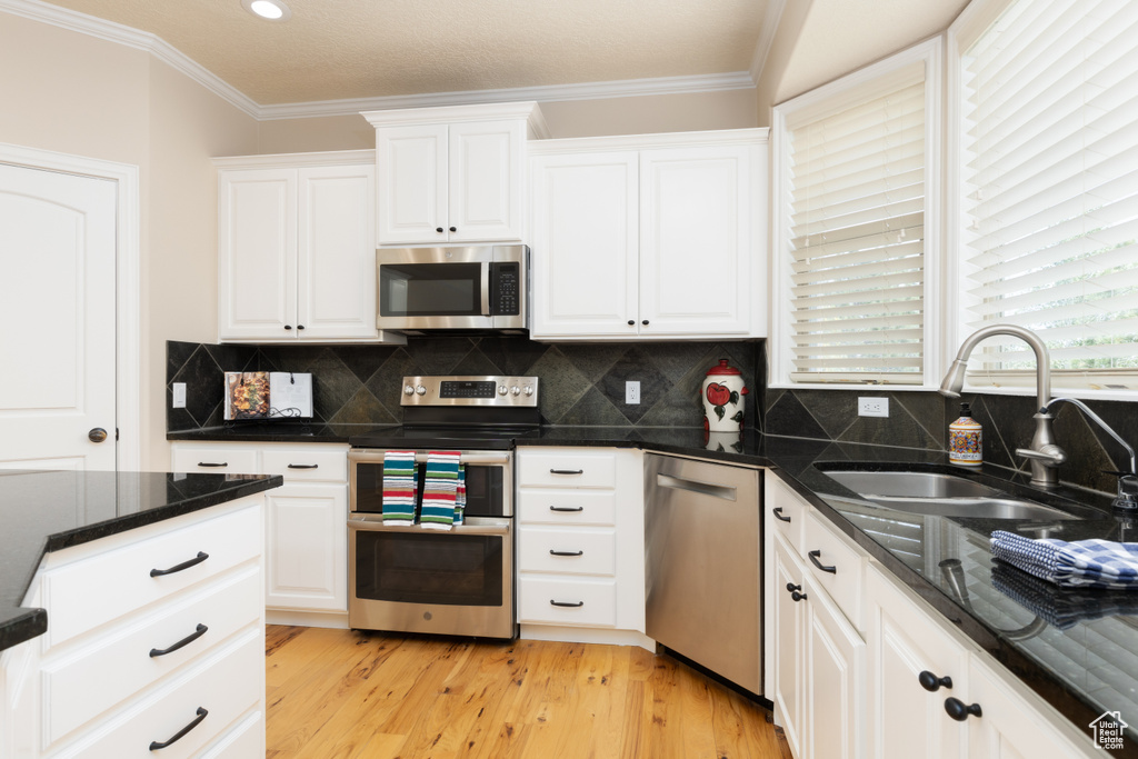 Kitchen with appliances with stainless steel finishes, a sink, white cabinetry, ornamental molding, and recessed lighting
