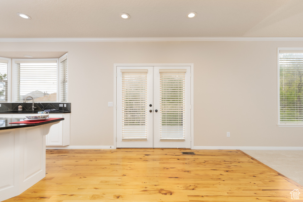 Unfurnished dining area with crown molding, french doors, healthy amount of natural light, light wood-type flooring, and recessed lighting