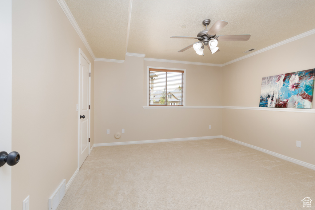 Spare room with light colored carpet, ceiling fan, crown molding, baseboards, and a textured ceiling