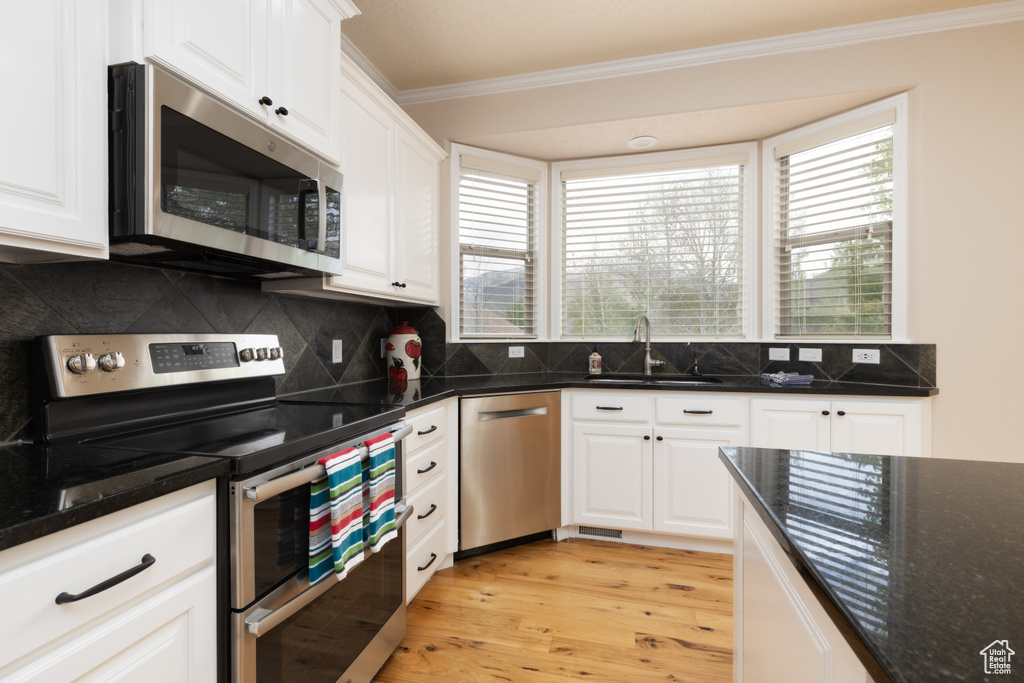 Kitchen featuring stainless steel appliances, a sink, ornamental molding, light wood finished floors, and white cabinetry