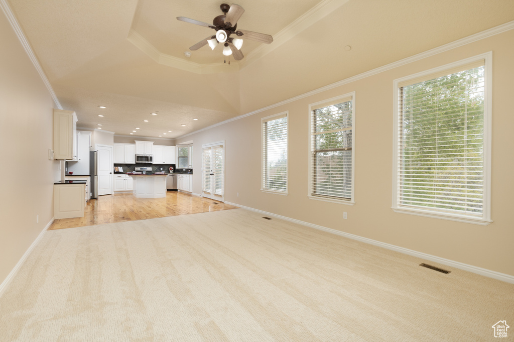 Unfurnished living room featuring light carpet, crown molding, a ceiling fan, healthy amount of natural light, and baseboards