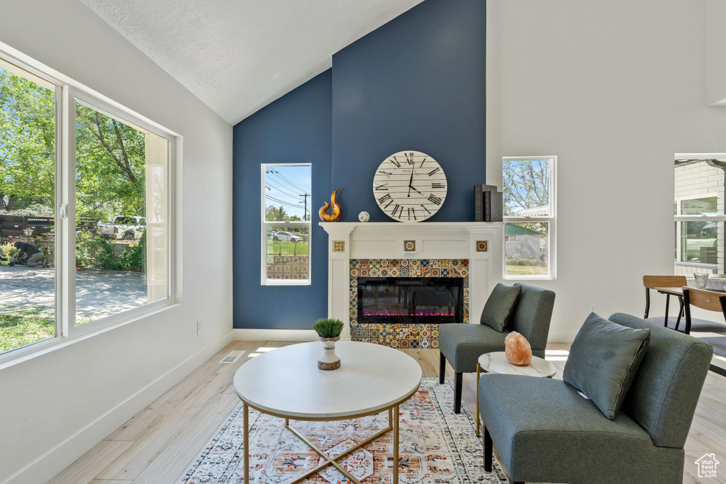 Living area with healthy amount of natural light, wood finished floors, high vaulted ceiling, baseboards, and a fireplace