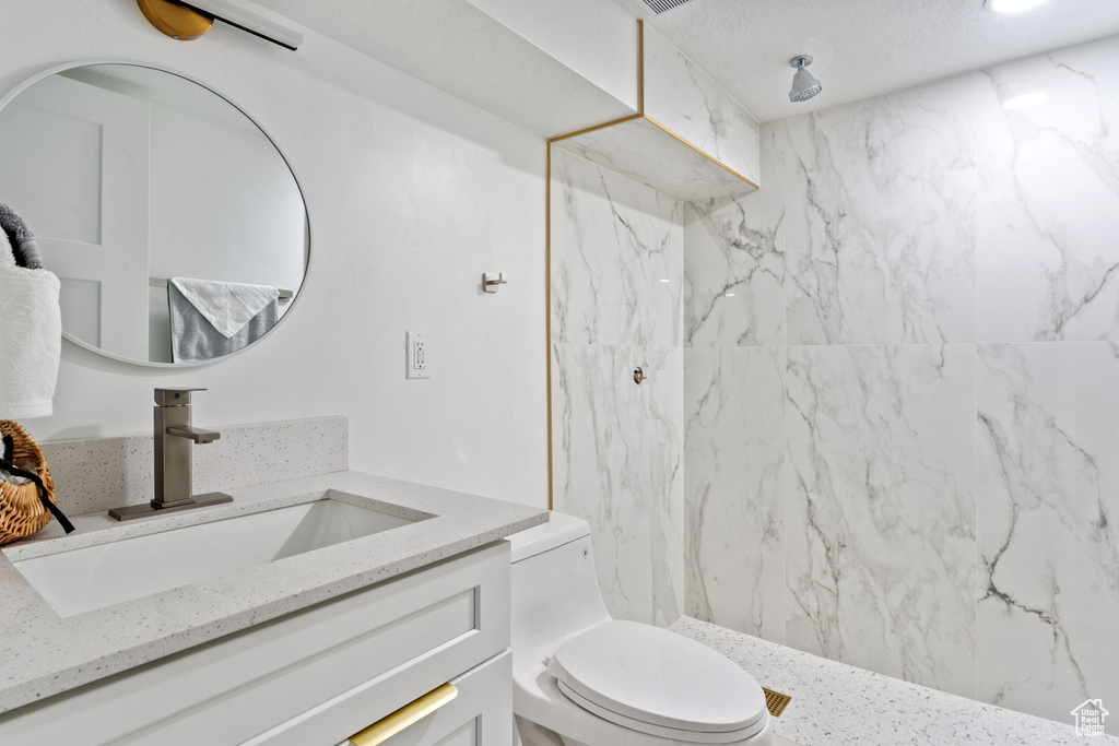 Full bath featuring vanity, a marble finish shower, and toilet
