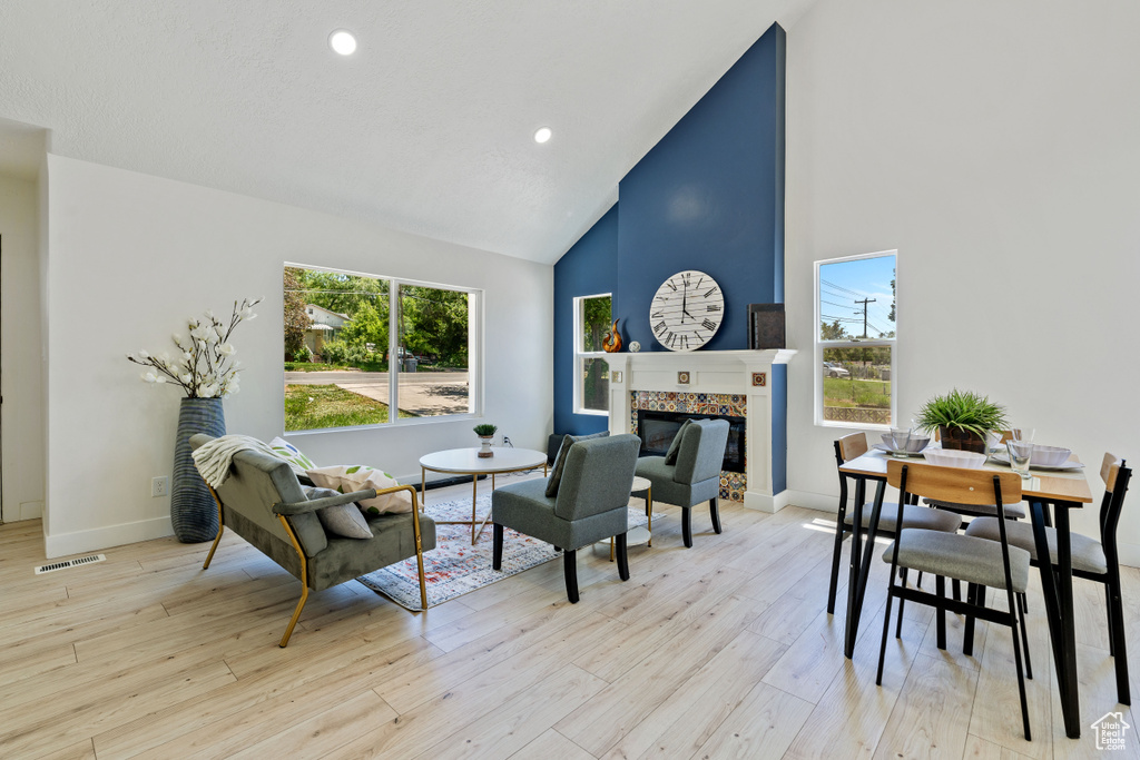 Living room with high vaulted ceiling, a tile fireplace, light wood-style flooring, baseboards, and recessed lighting