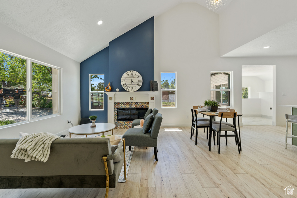 Living room with high vaulted ceiling, a fireplace, light wood-style floors, baseboards, and recessed lighting