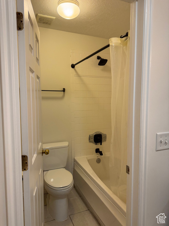 Bathroom with tile patterned floors, a textured ceiling, toilet, and shower / bathtub combination with curtain