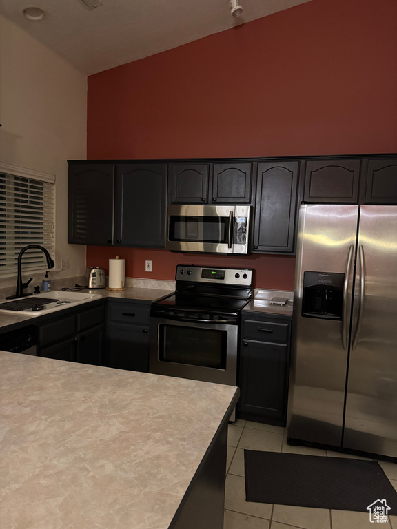 Kitchen with stainless steel appliances, a sink, high vaulted ceiling, light countertops, and light tile patterned floors