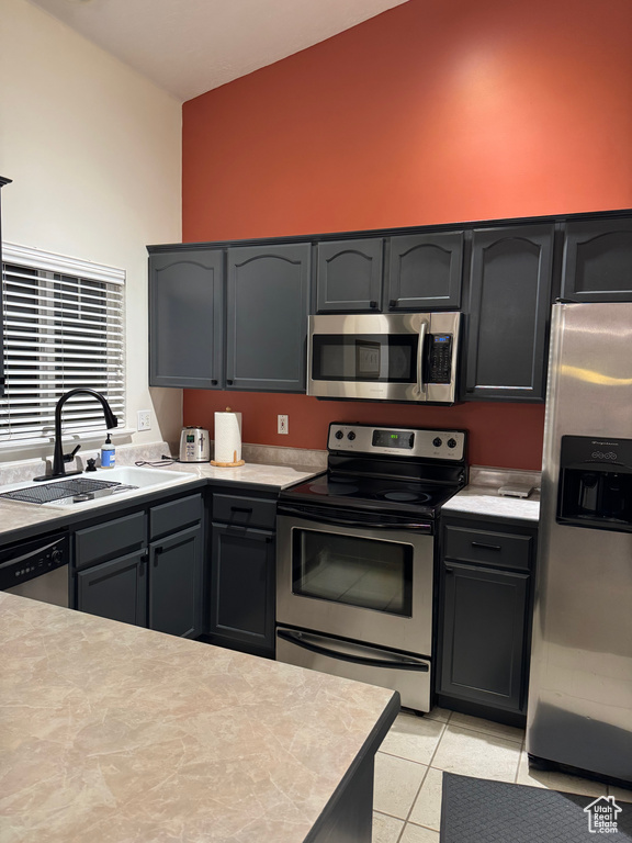 Kitchen featuring stainless steel appliances, a sink, light countertops, light tile patterned floors, and high vaulted ceiling