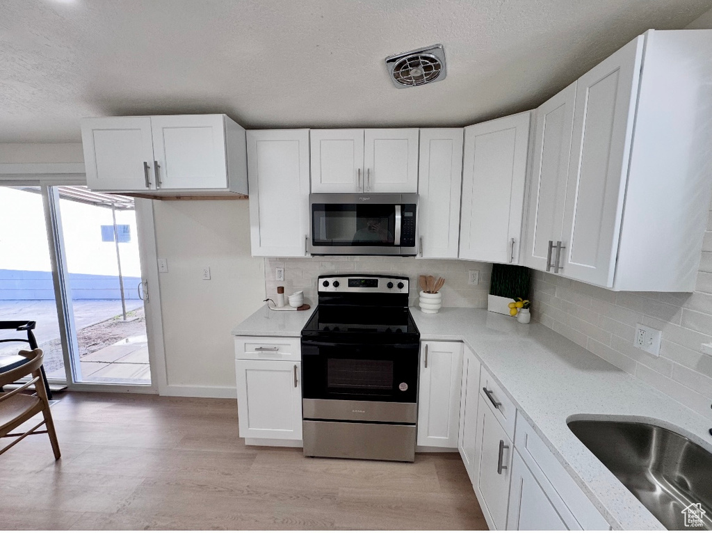 Kitchen featuring appliances with stainless steel finishes, a textured ceiling, white cabinets, decorative backsplash, and light wood finished floors