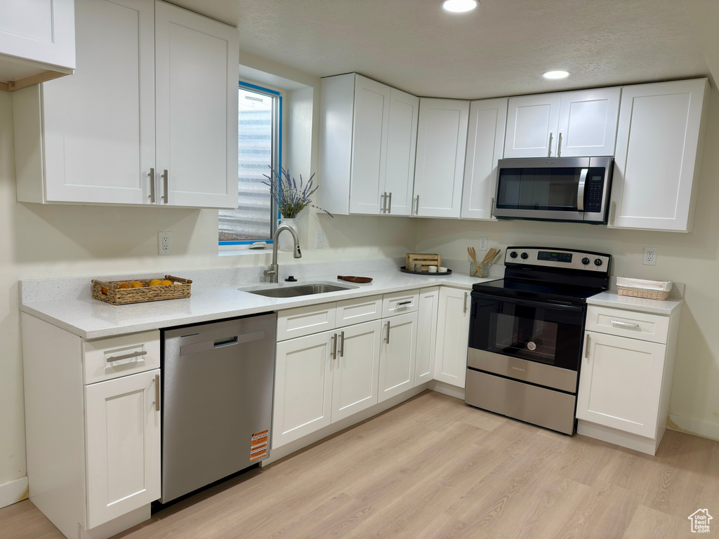Kitchen with stainless steel appliances, a sink, white cabinetry, light countertops, and light wood-style floors
