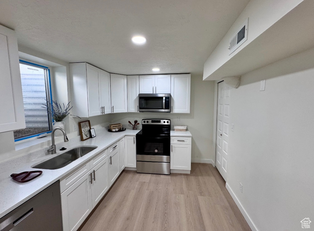 Kitchen with appliances with stainless steel finishes, a sink, light wood-style flooring, light countertops, and white cabinets