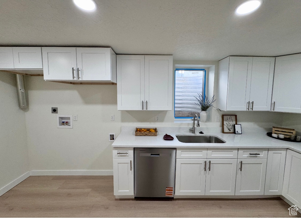 Kitchen featuring stainless steel dishwasher, a sink, white cabinetry, light wood-type flooring, and baseboards