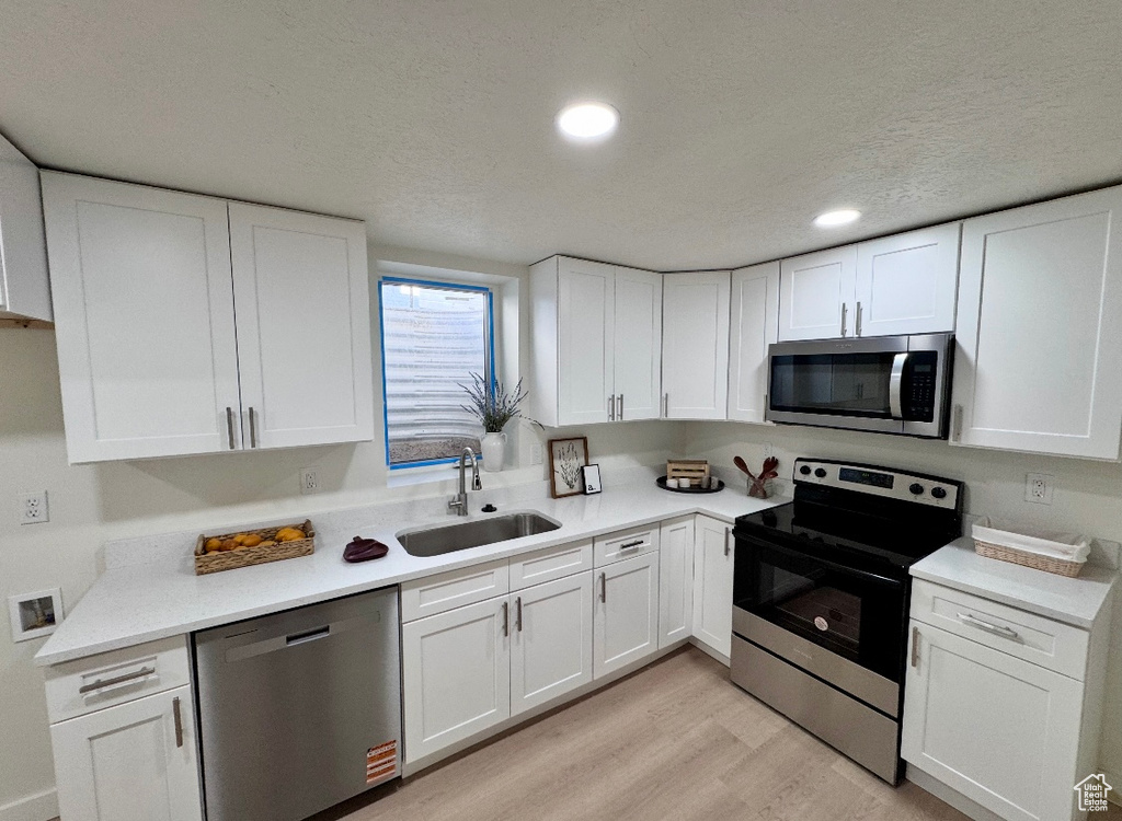 Kitchen with stainless steel appliances, a sink, white cabinets, light countertops, and recessed lighting