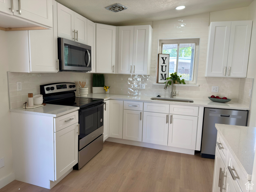 Kitchen with stainless steel appliances, a sink, white cabinets, light wood-style floors, and recessed lighting