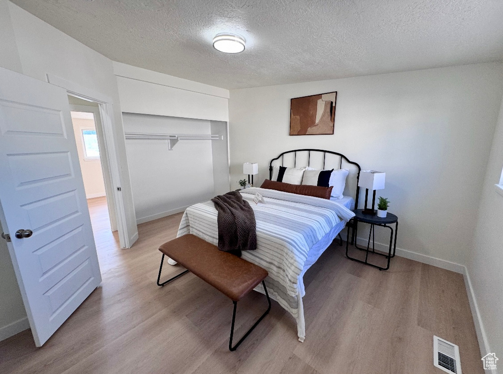 Bedroom featuring a textured ceiling, light wood-style flooring, baseboards, and a closet