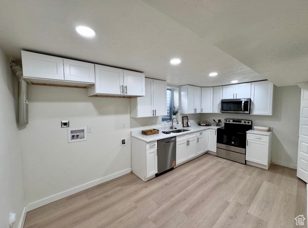 Kitchen featuring appliances with stainless steel finishes, light wood-style flooring, white cabinets, a sink, and baseboards