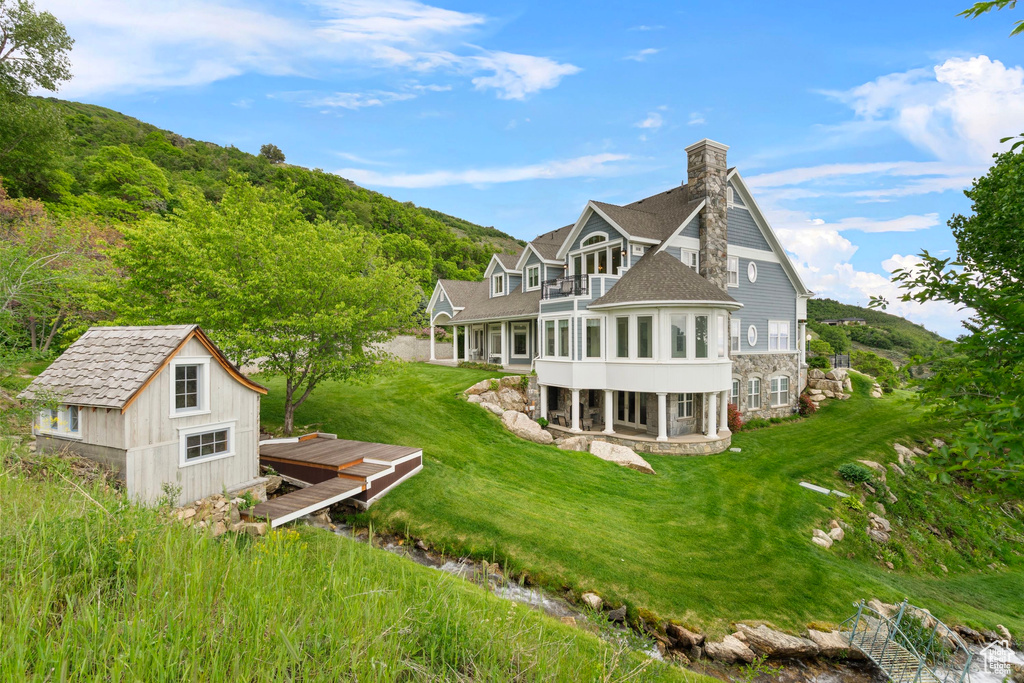 Back of house featuring a balcony, a chimney, a yard, stone siding, and a patio area