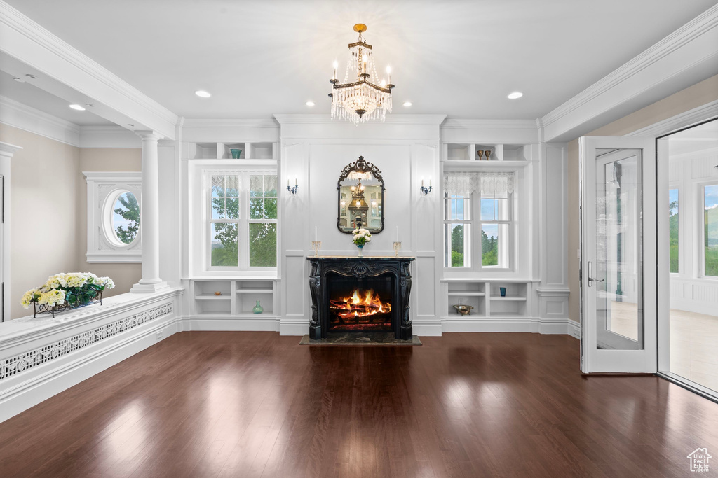 Unfurnished living room with decorative columns, wood finished floors, a warm lit fireplace, recessed lighting, and ornamental molding
