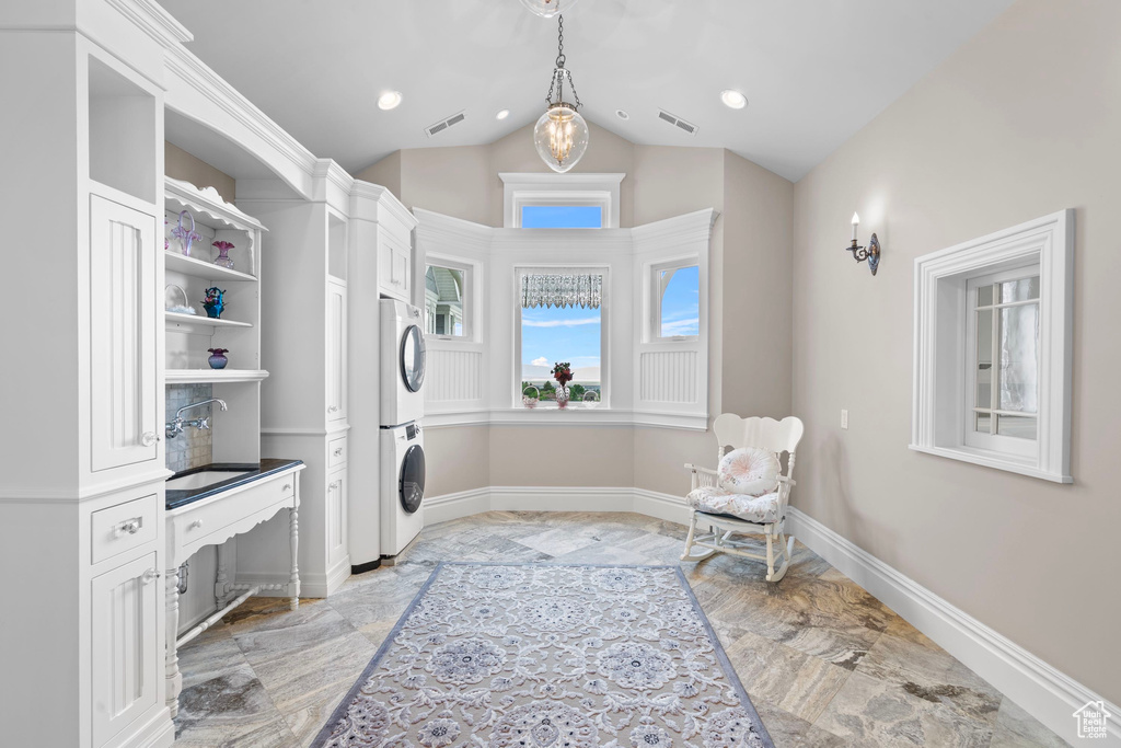 Laundry room with stacked washing machine and dryer, light marble finish flooring, baseboards, and recessed lighting