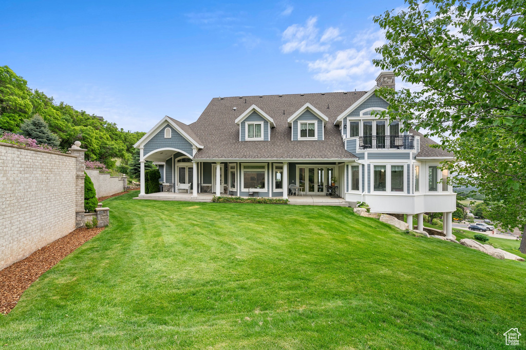 Rear view of property with a balcony, a yard, a shingled roof, and french doors