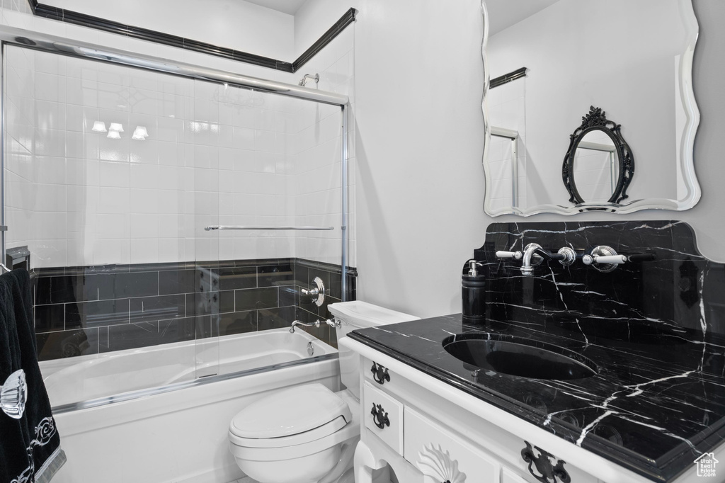 Full bath with bath / shower combo with glass door, toilet, and vanity