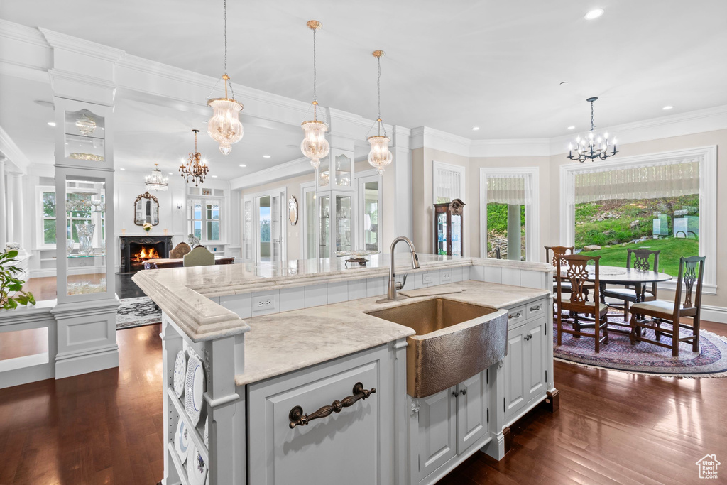 Kitchen featuring a sink, a chandelier, a warm lit fireplace, dark wood-style floors, and recessed lighting