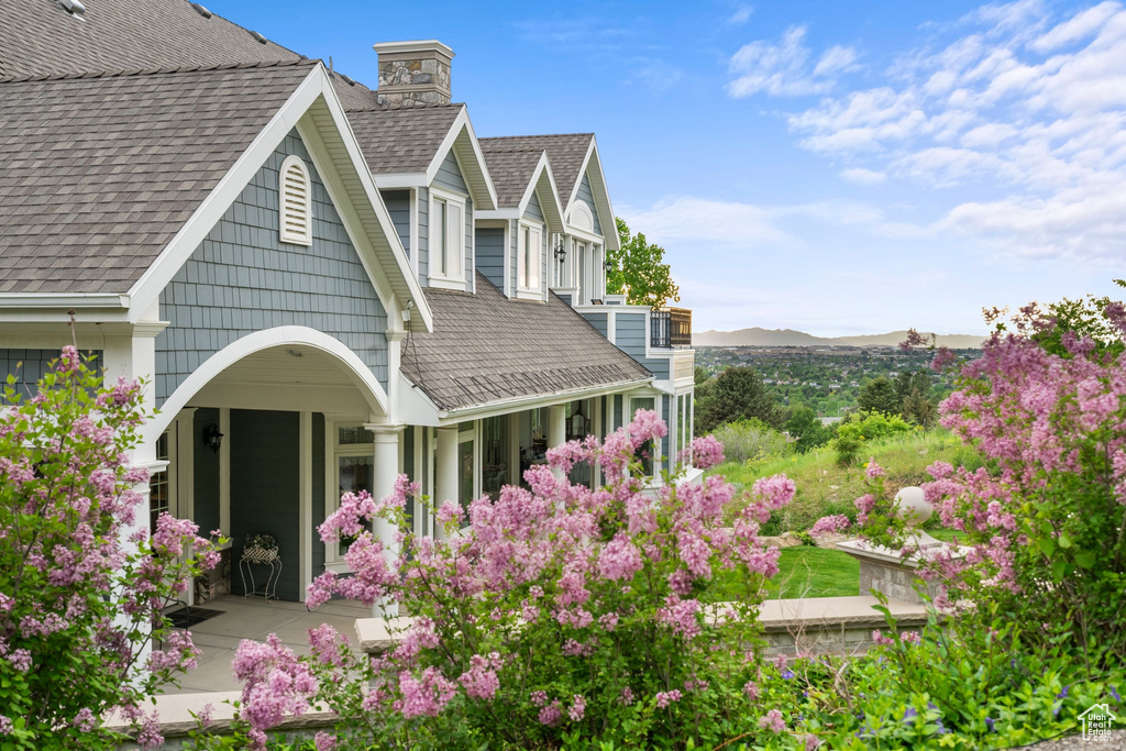 Rear view of house featuring roof with shingles, a chimney, a mountain view, and a porch