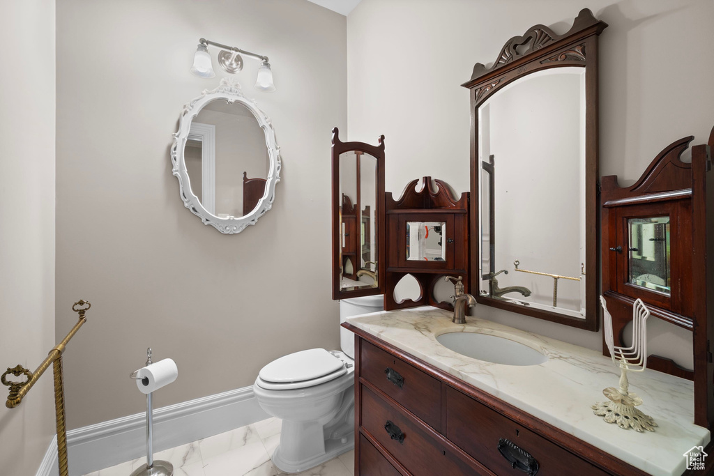 Half bath featuring marble finish floors, toilet, baseboards, and vanity