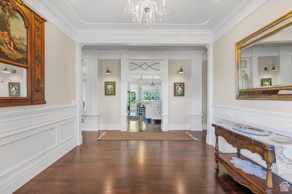 Entrance foyer featuring decorative columns, dark wood-style flooring, crown molding, a decorative wall, and a wainscoted wall