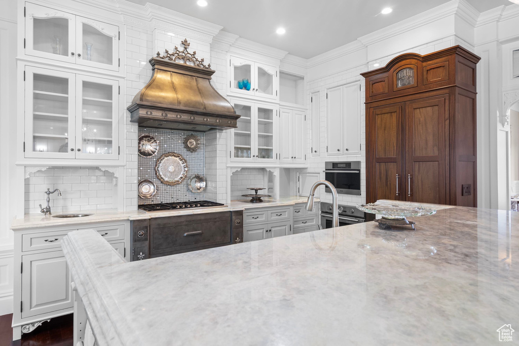 Kitchen featuring a sink, stainless steel appliances, glass insert cabinets, custom range hood, and white cabinets