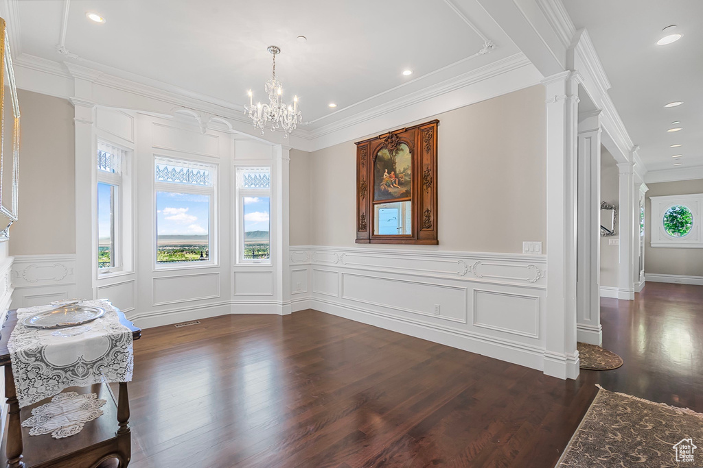 Unfurnished dining area featuring decorative columns, dark wood-style flooring, a chandelier, recessed lighting, and a wainscoted wall