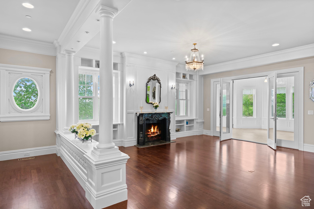 Unfurnished living room featuring ornate columns, dark wood-style flooring, baseboards, ornamental molding, and recessed lighting