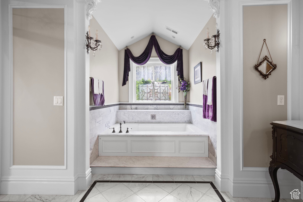 Bathroom featuring marble look tile flooring, a garden tub, and lofted ceiling