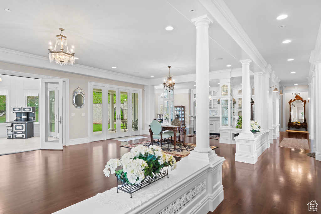 Living room with a chandelier, decorative columns, dark wood-type flooring, ornamental molding, and french doors