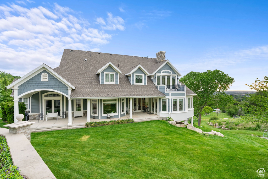 Rear view of house with a balcony, french doors, a lawn, a chimney, and roof with shingles