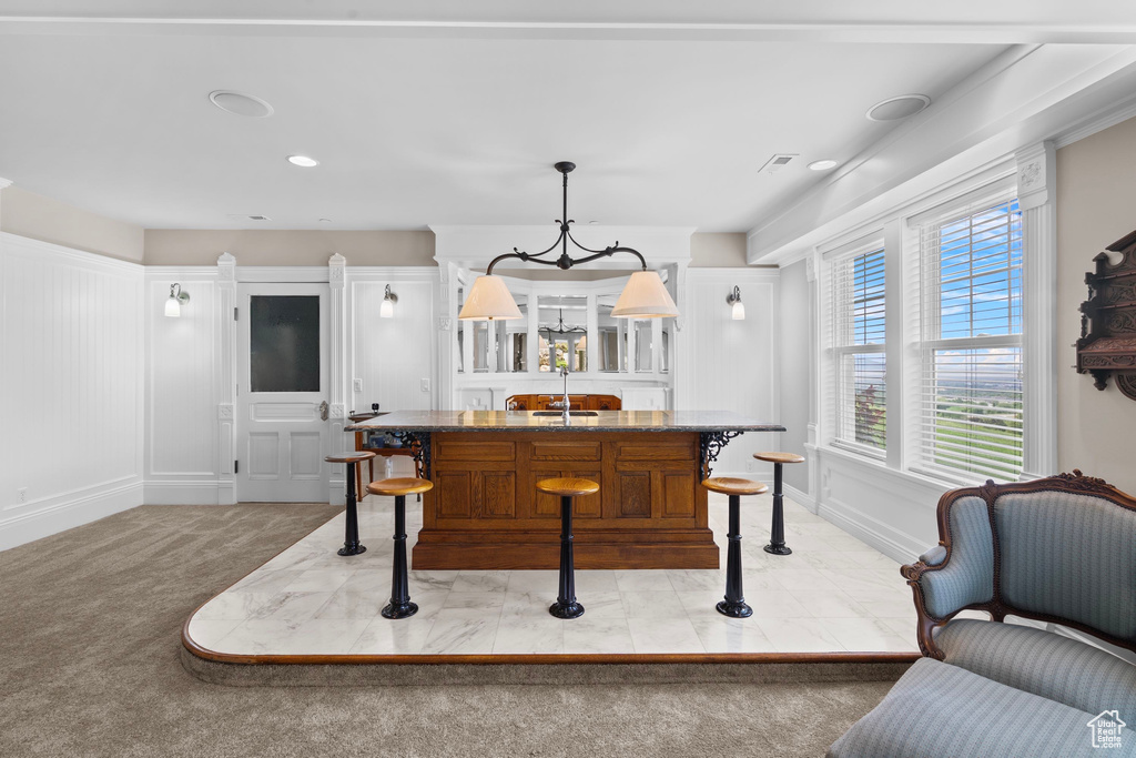 Kitchen featuring a sink, a chandelier, a kitchen island with sink, light colored carpet, and pendant lighting