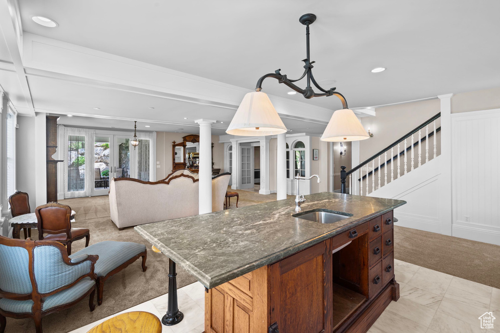 Kitchen with a sink, dark stone counters, a center island with sink, pendant lighting, and decorative columns
