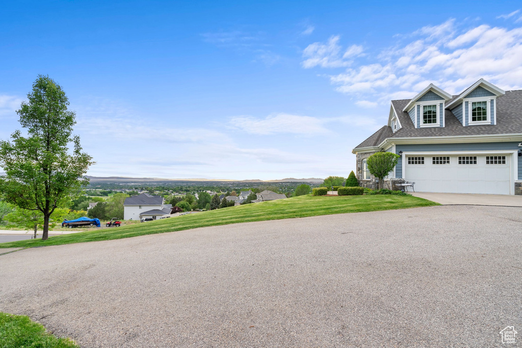 View of side of home featuring driveway, a garage, a yard, and a shingled roof