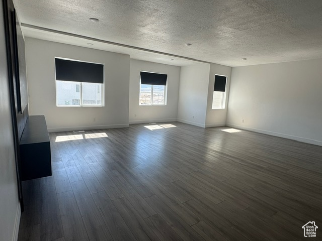 Spare room with a textured ceiling, dark wood-style flooring, and baseboards