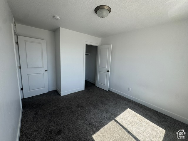Unfurnished bedroom featuring dark colored carpet, baseboards, a textured ceiling, and a closet