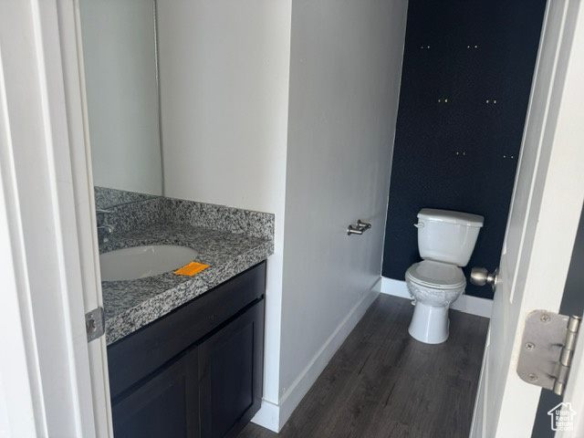 Half bathroom featuring toilet, vanity, baseboards, and wood finished floors
